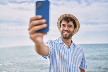 Genç İspanyol gülümseyen adam sahildeki akıllı telefonun yanında selfie çekerken mutlu oluyor.