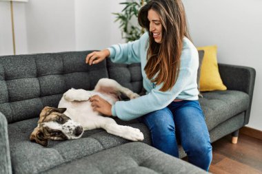 Evdeki kanepede köpekle oynayan genç bir kadın.
