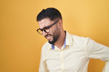 İspanyol genç adam iş kıyafetleri ve gözlük takıyor sırt ağrısı çekiyor, elleriyle dokunuyor, kas ağrısı çekiyor. 