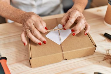 Kıdemli gri saçlı iş kadını ofiste paket siparişi hazırlıyor.
