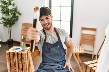 Genç İspanyol sanatçı gülümsüyor. Resim stüdyosunda fırça tutarken mutlu..