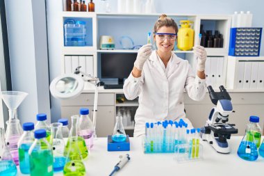 Laboratuvarda test tüpleri tutan bilim adamı üniforması giyen genç sarışın kadın.