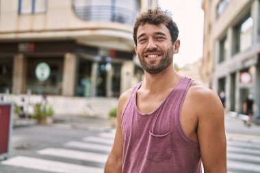 Genç İspanyol adam gülümseyerek şehirde mutlu mesut dikiliyor..