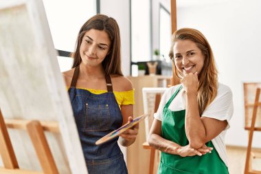 Anne ve kızı resim stüdyosunda kendine güvenen bir şekilde gülümsüyor.