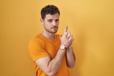 Sarı arka planda duran İspanyol genç adam sembolik bir silahla el hareketleriyle cinayet silahlarıyla oynuyor, kızgın surat. 