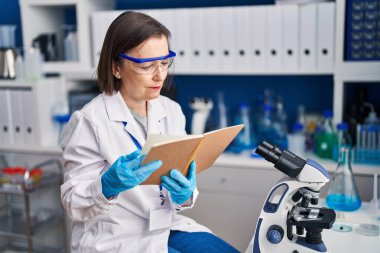 Laboratuvarda kitap okuyan orta yaşlı kadın bilim adamı.