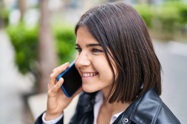 Genç, güzel, İspanyol bir kadın gülümsüyor ve caddede akıllı telefondan konuşuyor.