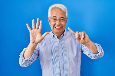 Hispanic senior man wearing glasses showing and pointing up with fingers number six while smiling confident and happy. 
