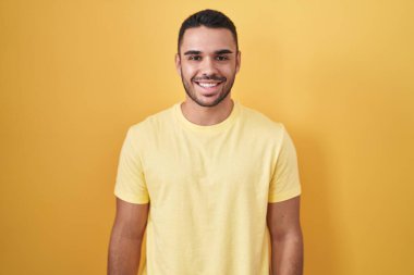 Yüzünde mutlu ve havalı bir gülümsemeyle sarı arka planda duran İspanyol genç adam. şanslı kişi. 