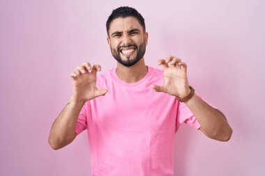 İspanyol genç adam pembe arka planda durup gülümsüyor. Pençe hareketini kedi gibi yapıyor. Agresif ve seksi bir ifade. 