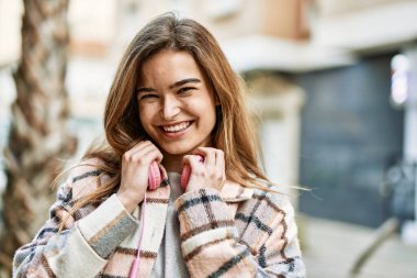 Kulaklık takan genç sarışın kadın sokakta kendinden emin gülümsüyor.