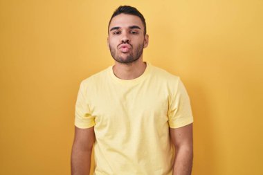 Latin asıllı genç adam sarı arka planda duruyor ve kameraya bakıyor. Canlı yayında öpücük yolluyor. Güzel ve seksi. aşk ifadesi. 