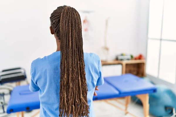 Black woman with braids working at pain recovery clinic standing backwards looking away with crossed arms