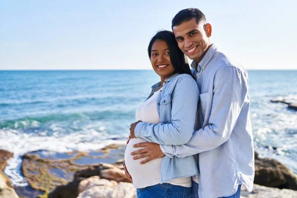 Young Latin Couple Expecting Baby Hugging Each Other Standing Seaside — Stockfoto