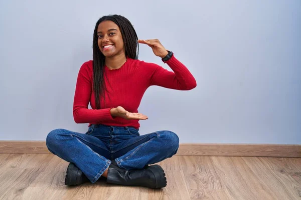Młody Afroamerykanin Warkoczami Siedzący Podłodze Domu Gestykulujący Rękami Pokazującymi Duży — Zdjęcie stockowe