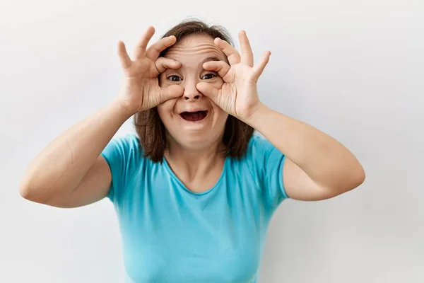 孤立した背景の上に立つ若いダウン症候群の女性は 双眼鏡の舌を突き出すようなOkジェスチャーをして 目を指で見ている クレイジーな表現 — ストック写真