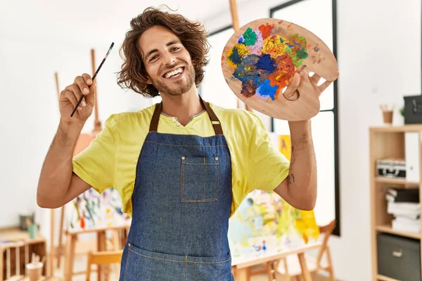 在艺术工作室拿着画笔和调色板时 他那年轻的惊慌失措的艺术家高兴地微笑着 — 图库照片