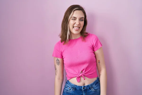 ピンク色の背景に立っているブロンドの白人女性が面白い表情で幸せ舌を突き出しています 感情の概念 — ストック写真