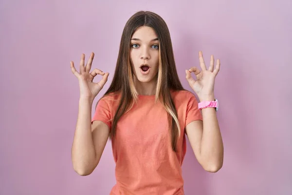 站在粉色背景上的少女看上去很惊讶 很震惊用手指做了个认可的符号 疯狂的表达 — 图库照片