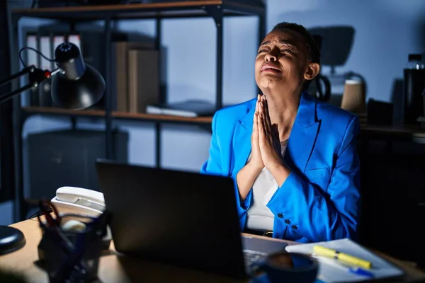 Beautiful african american woman working at the office at night begging and praying with hands together with hope expression on face very emotional and worried. begging.