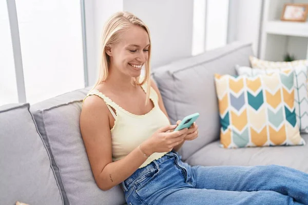 Evdeki Kanepede Oturan Akıllı Telefon Kullanan Genç Sarışın Kadın — Stok fotoğraf