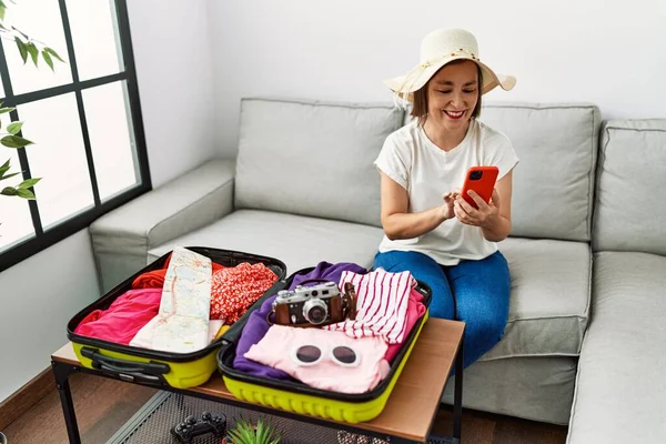 Middle Age Hispanic Woman Packing Holidays Using Smartphone Home — Stockfoto