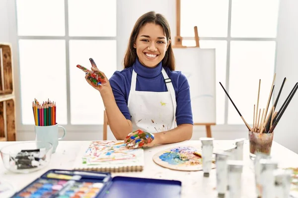 在艺术工作室里 年轻的黑发女人 手绘彩绘 满脸喜色 微笑着看着相机做胜利的标志 第二点 — 图库照片