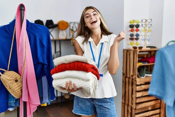 Young Blonde Woman Working Manager Retail Boutique Holding Sweaters Screaming — Stock Photo, Image