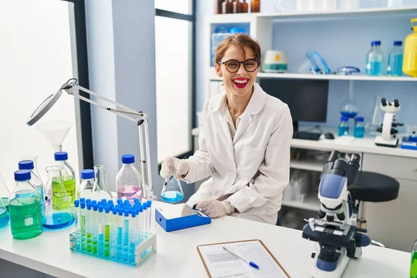 Young Caucasian Woman Wearing Scientist Uniform Measuring Liquid Laboratory — стоковое фото