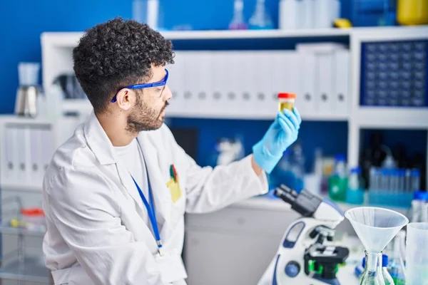 Laboratuvarda idrar tüpü tutan bilim adamı üniforması giyen genç bir Arap.
