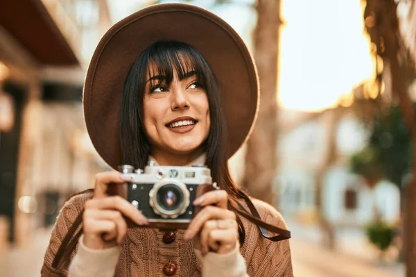 冬の帽子を身に着けているブルネットの女性は 市内の屋外でヴィンテージカメラを使用して笑顔 — ストック写真