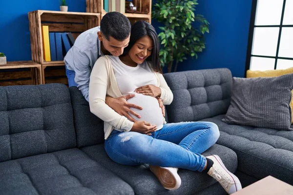 Young Latin Couple Expecting Baby Hugging Each Other Sitting Sofa — Foto Stock