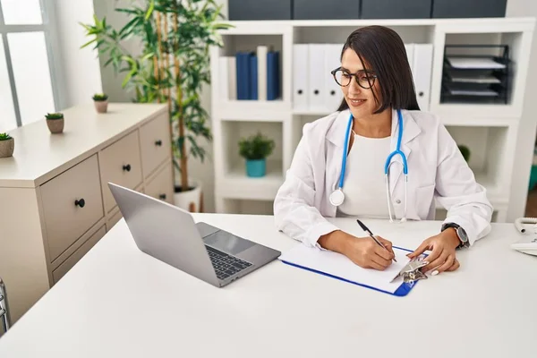 Young Hispanic Woman Wearing Doctor Uniform Writing Clipboard Clinic — Stock Photo, Image