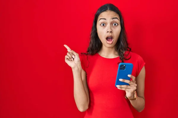 Jeune Femme Brésilienne Utilisant Smartphone Sur Fond Rouge Surpris Pointant — Photo