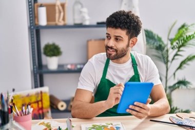 Genç Arap sanatçı, sanat stüdyosunda dokunmatik ped kullanarak gülümsüyor.