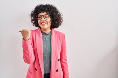 Kıvırcık saçlı İspanyol kadın izole edilmiş arka planda gülümsüyor, gülümsüyor ve başparmağıyla yan tarafı işaret ediyor.. 