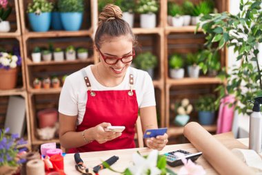 Çiçekçide akıllı telefon ve kredi kartı kullanan güzel İspanyol bir çiçekçi.