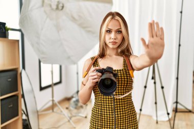 Kafkasyalı genç fotoğrafçı kız elinde profesyonel kamerayla fotoğraf stüdyosunda dur işareti yapıyor ciddi ve kendinden emin bir ifadeyle, savunma jesti yapıyor. 