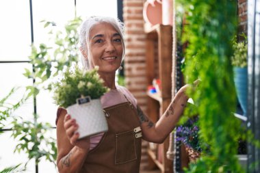 Çiçekçiye saksı tutan kır saçlı kadın çiçekçi.