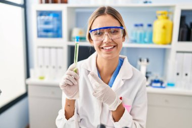Laboratuvarda çalışan genç sarışın kadın elinde numune tutarak gülümsüyor. 