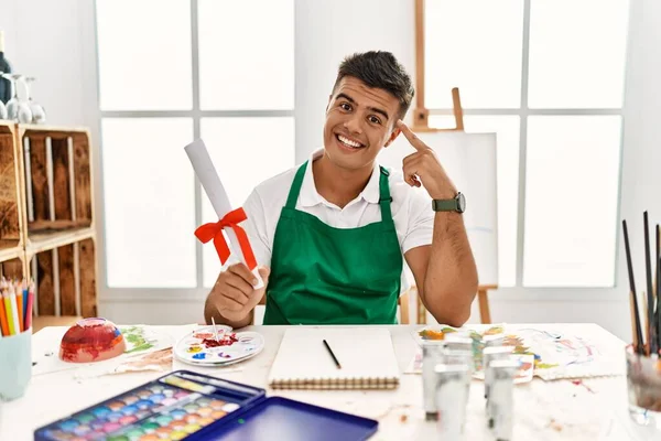 Joven Hombre Hispano Estudio Arte Sosteniendo Grado Sonriendo Apuntando Cabeza — Foto de Stock