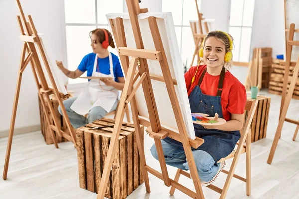 Two artist student women smiling happy and listening to music painting at art school.