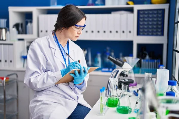 Young woman scientist writing on notebook at laboratory