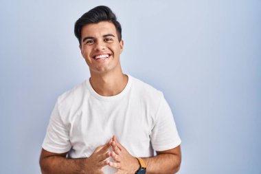 Mavi arka planda dikilen İspanyol adam ellerini birleştirip gülümseyerek gevşemiş ve neşeli olmasını diledi. Başarı ve iyimserlik 