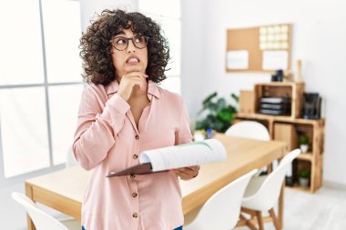 Ofiste iş elbisesi giyen genç bir ortadoğulu kadın bir soru hakkında endişeli ve gergin bir şekilde düşünüyor. 