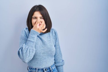 Mavi arka planda dikilen genç İspanyol kadın pis ve iğrenç bir koku alıyor. Nefesini burnunda tutuyor. Kötü kokuyor. 