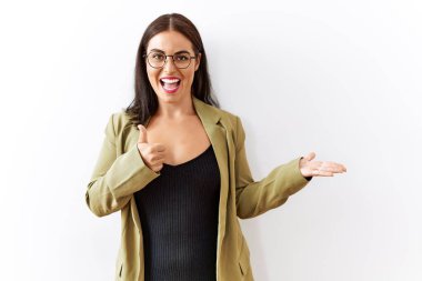 Genç esmer kadın izole edilmiş arka planda duruyor. Avuç içlerini gösteriyor ve baş parmaklarıyla iyi bir hareket yapıyor. Mutlu ve neşeli gülümsüyor. 