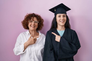 Latin kökenli anne ve kız mezuniyet şapkası ve tören cübbesi takıyor. Yüzünde mutlu ve doğal bir ifadeyle, elleri ve parmaklarıyla yüzünü gösteren bir gülümseme var. 