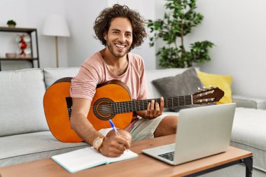 Genç İspanyol besteci evde gitar ve dizüstü bilgisayar kullanarak beste yapıyor..