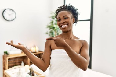 Genç Afro-Amerikan kadın havluyla güzellik merkezinde durup hayrete düşmüş ve kameraya gülümsüyor.. 